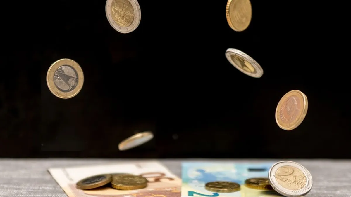 Dynamic image of euro coins and banknotes cascading onto a table against a black background.