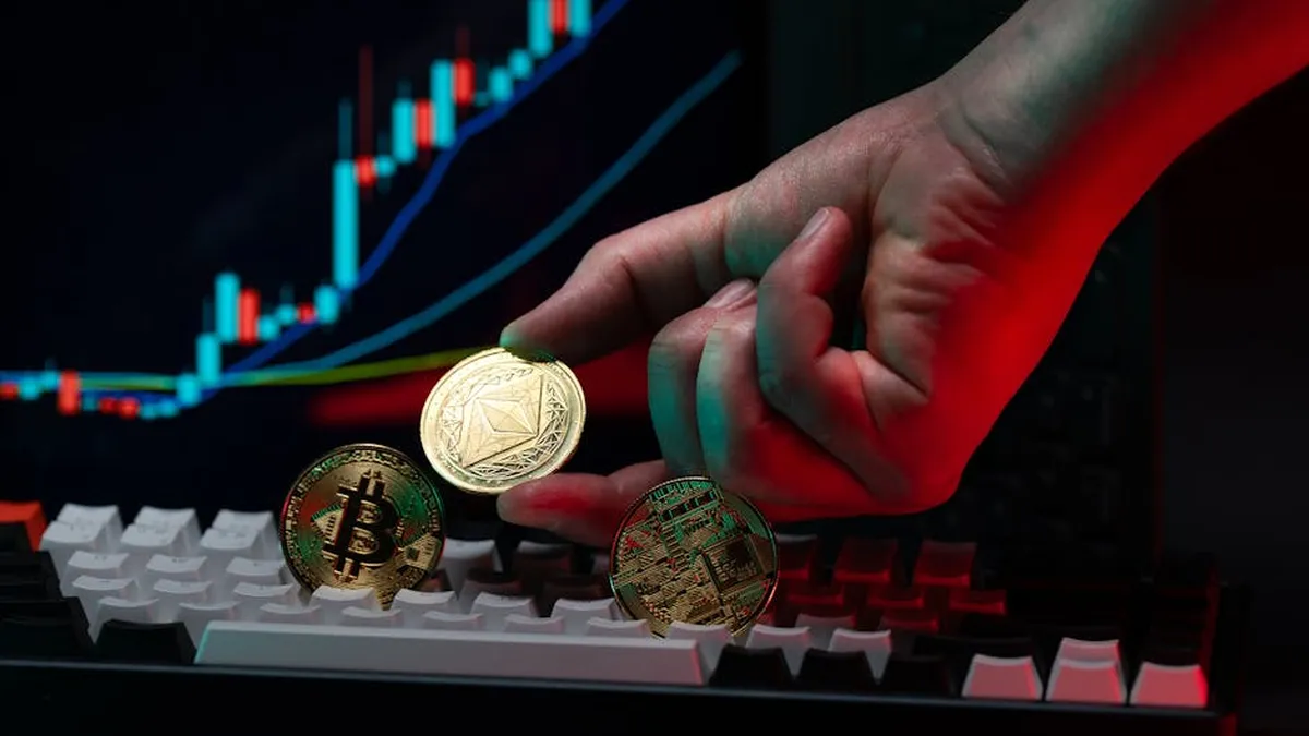 Close-up of a hand holding cryptocurrency coins on keyboard, with a graph display in the background.