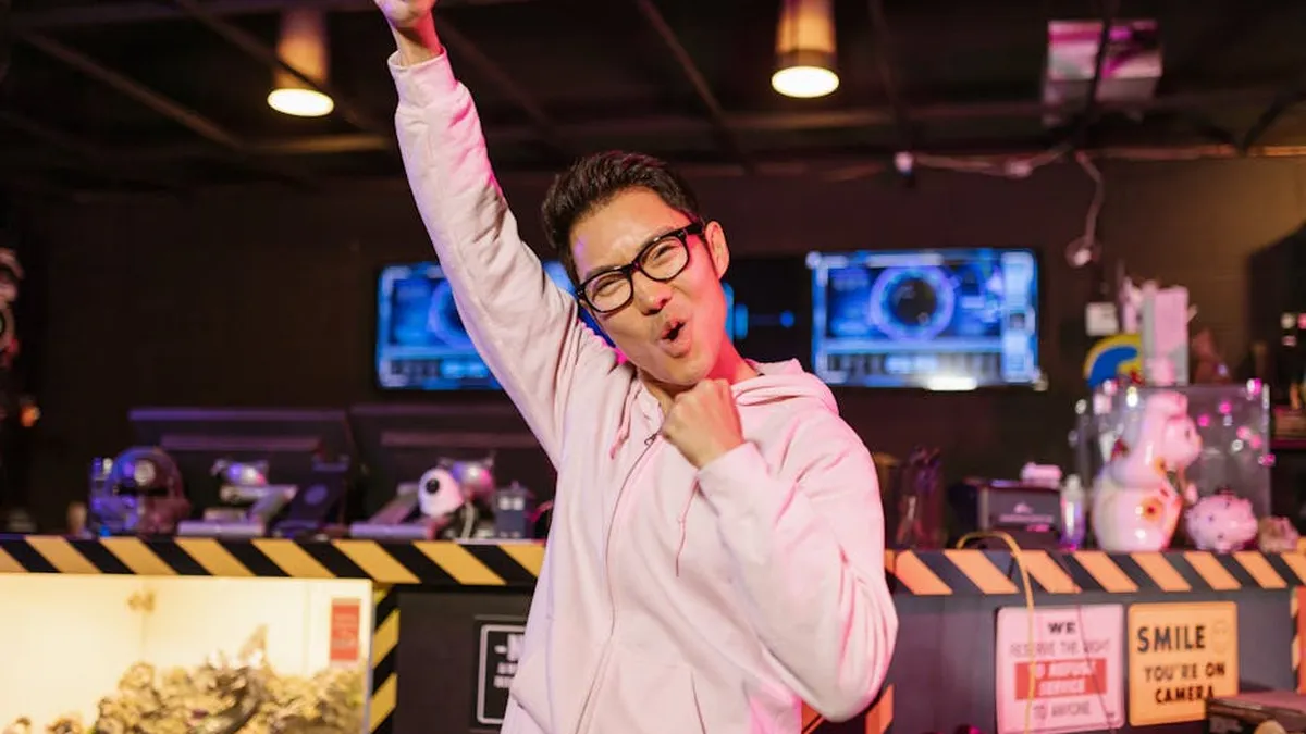 A cheerful gamer in a pink hoodie celebrating victory with a smiling face indoors.