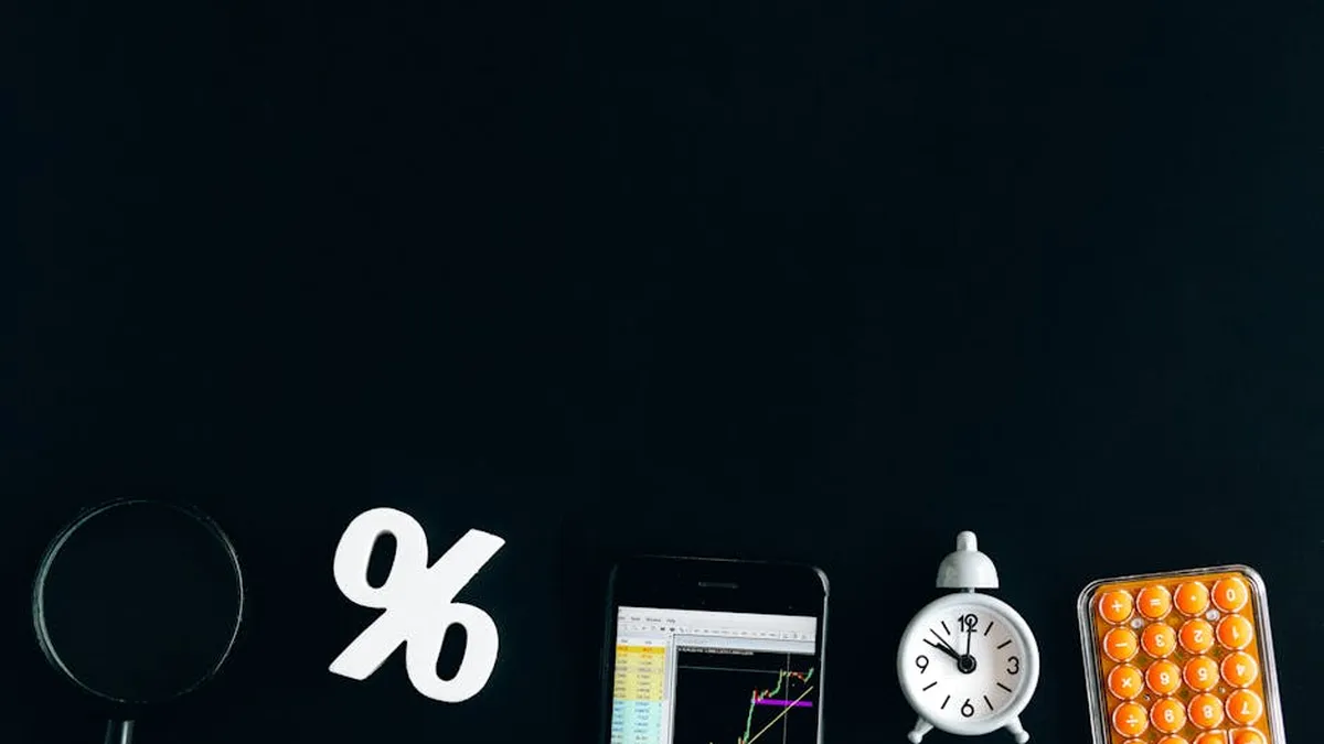 Flat lay of financial analysis tools including phone, clock, and calculator on black background.