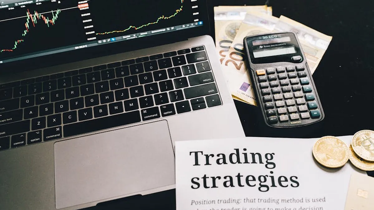 Close-up image of a trading setup with a laptop, calculator, and financial documents, ideal for finance and stock market themes.