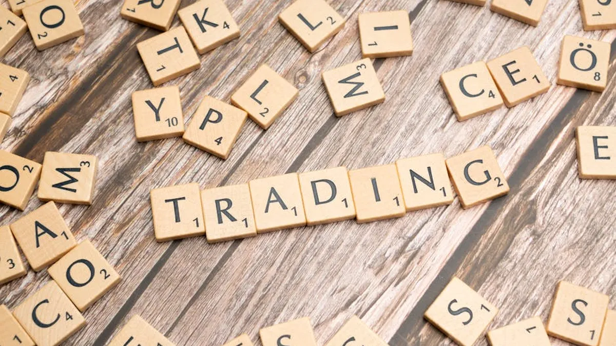 Wooden Scrabble tiles spelling 'TRADING' against a rustic wood background.