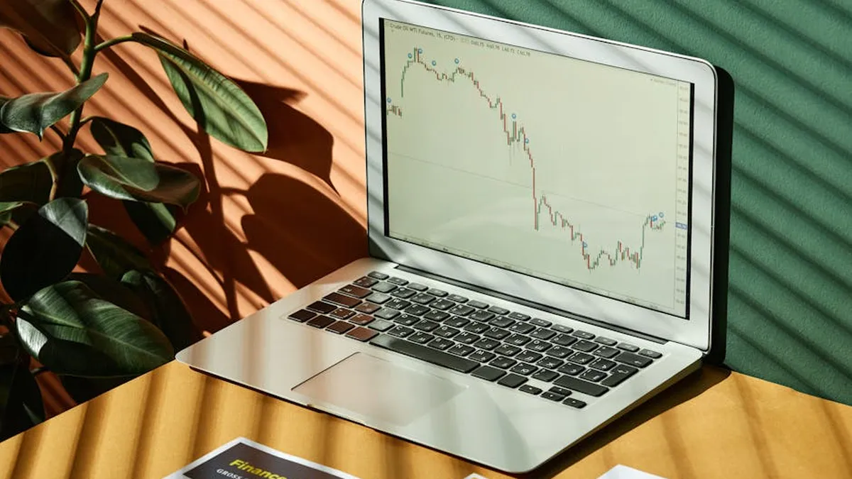 Laptop displaying a financial graph with reports, in a sunlit workspace.