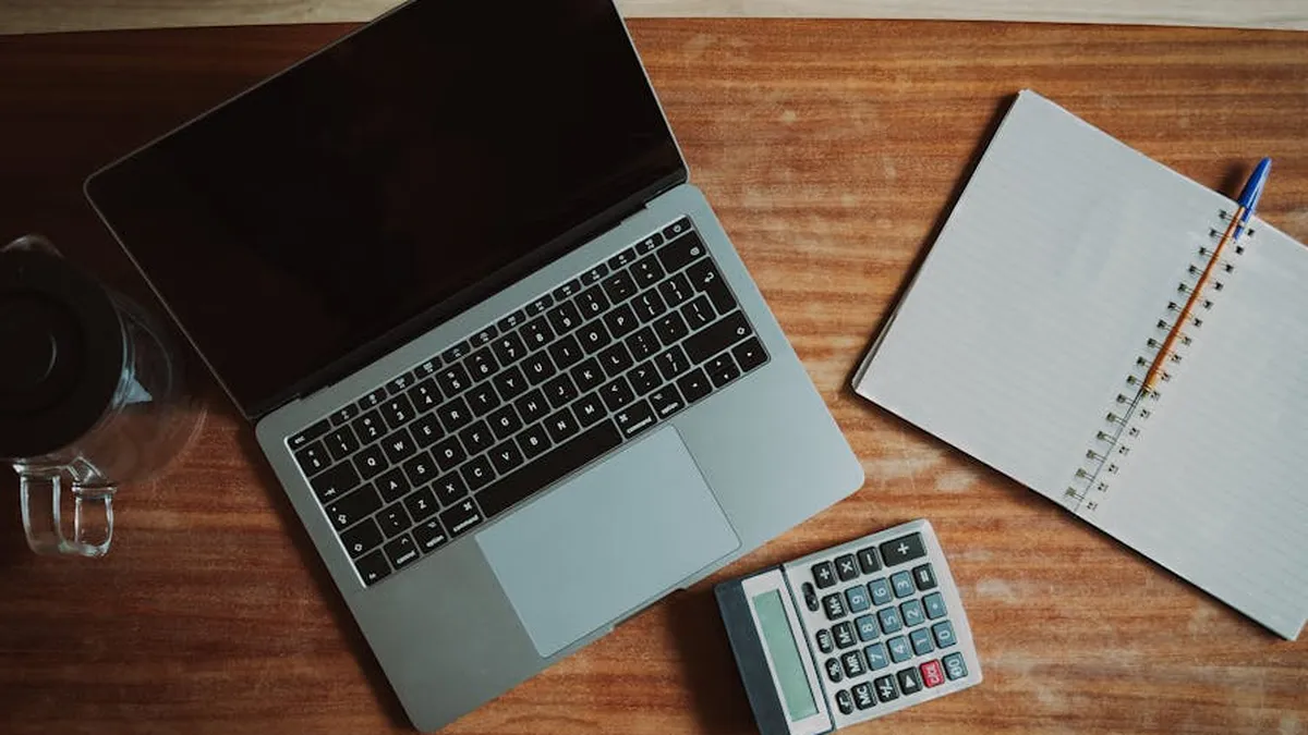 Top view of a desk with a laptop, calculator, and open notepad for work or study.