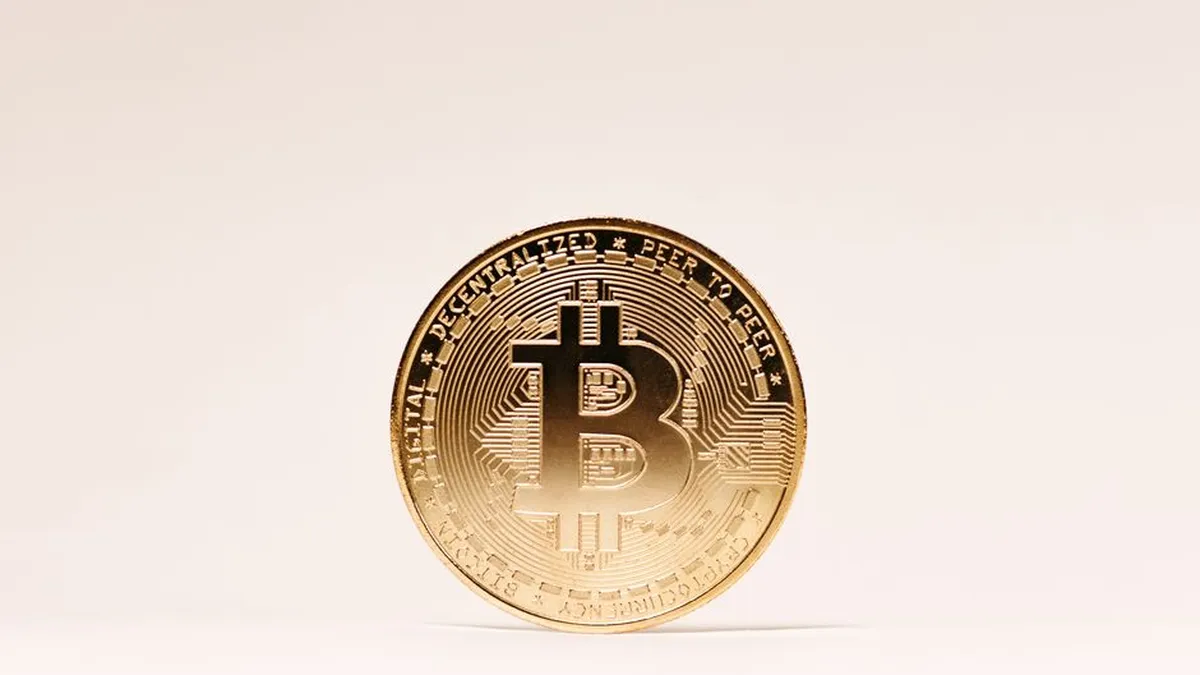 A golden Bitcoin coin standing upright against a minimalist light background.