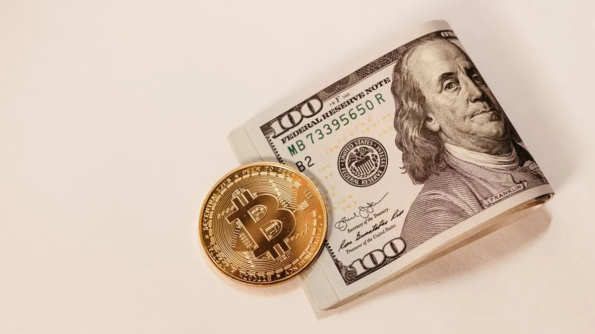 A Bitcoin coin placed next to a rolled US hundred dollar bill, symbolizing cryptocurrency and traditional currency.