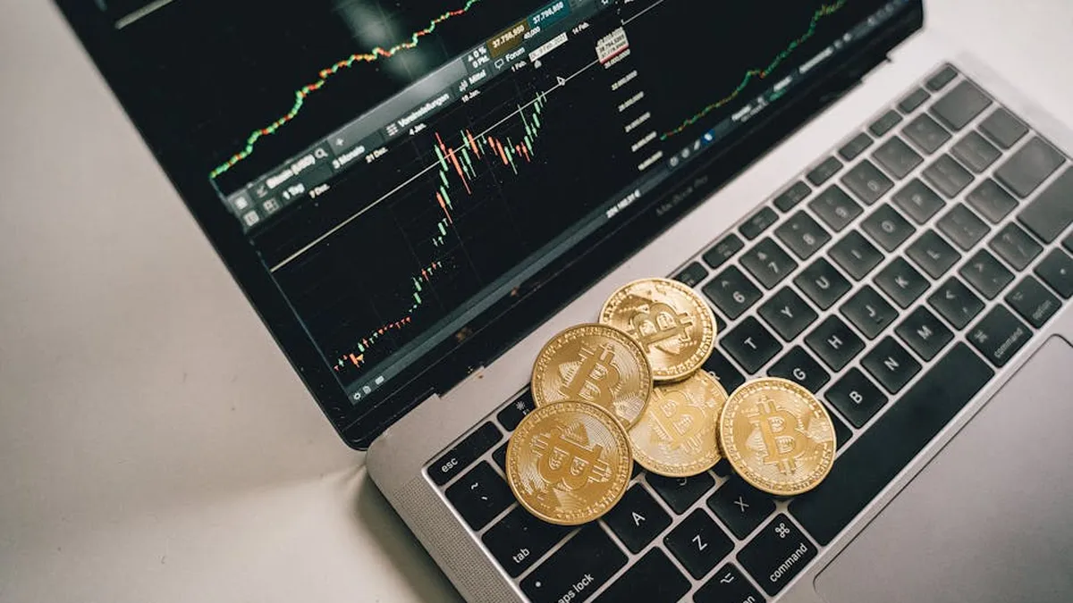 Golden bitcoin coins placed on a laptop keyboard with trading chart displayed on the screen.