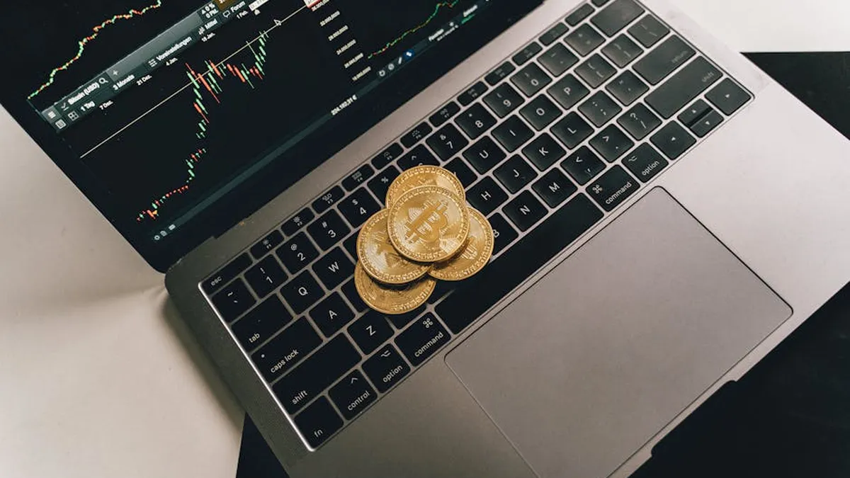 Bitcoin coins placed on a laptop keyboard while a trading chart displays on the screen, showcasing digital finance.