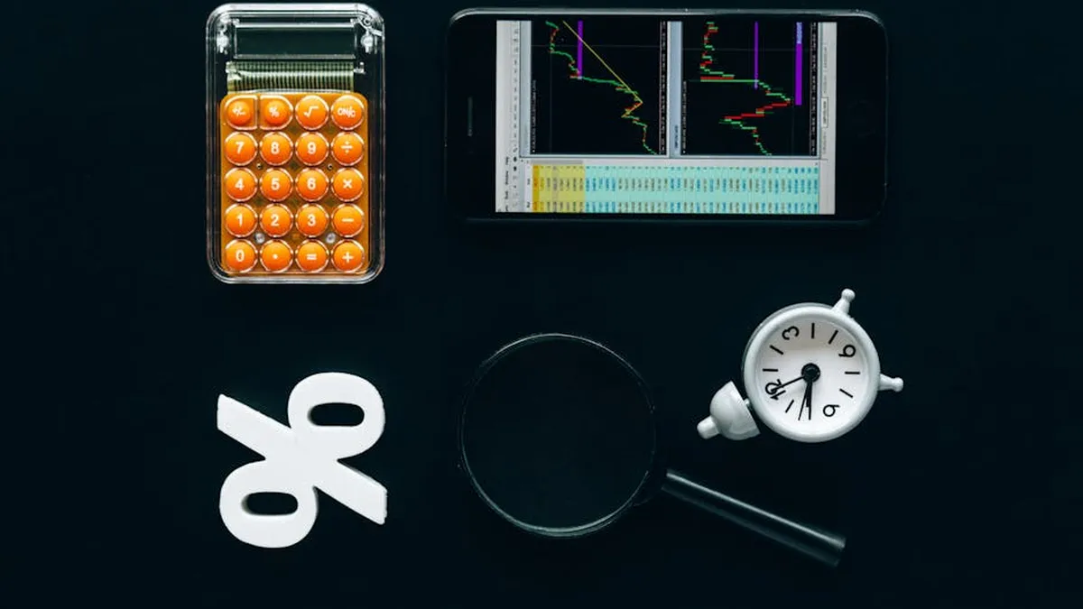 Top view of business tools including a calculator, smartphone with charts, magnifying glass, and clock on black background.
