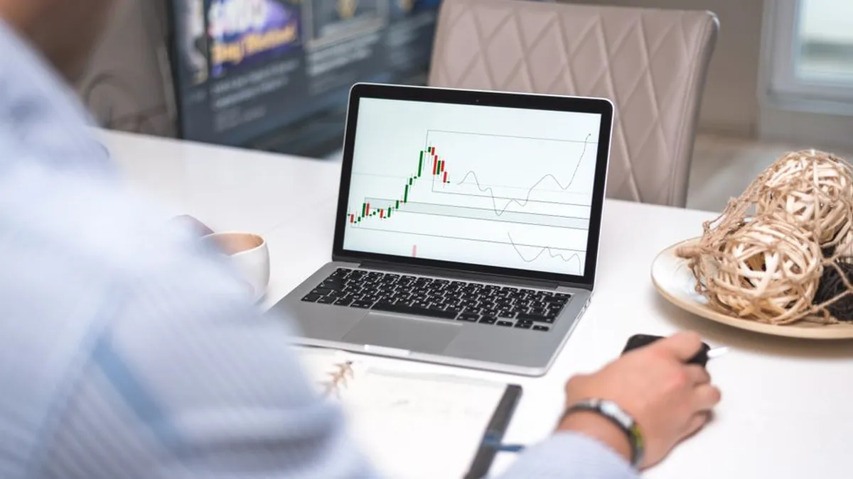 Man reviewing financial analysis on laptop in a modern office setting with focus on trading charts and data.