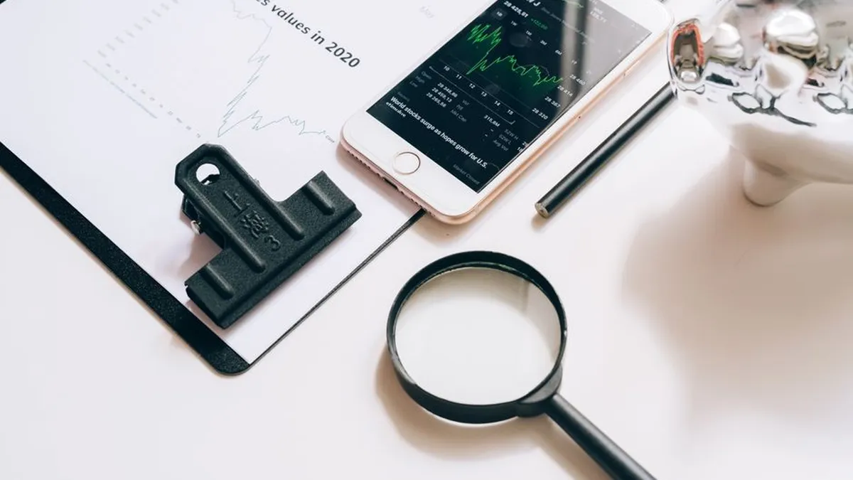 Flat lay of financial tools including a smartphone with stock data, magnifying glass, and chart.