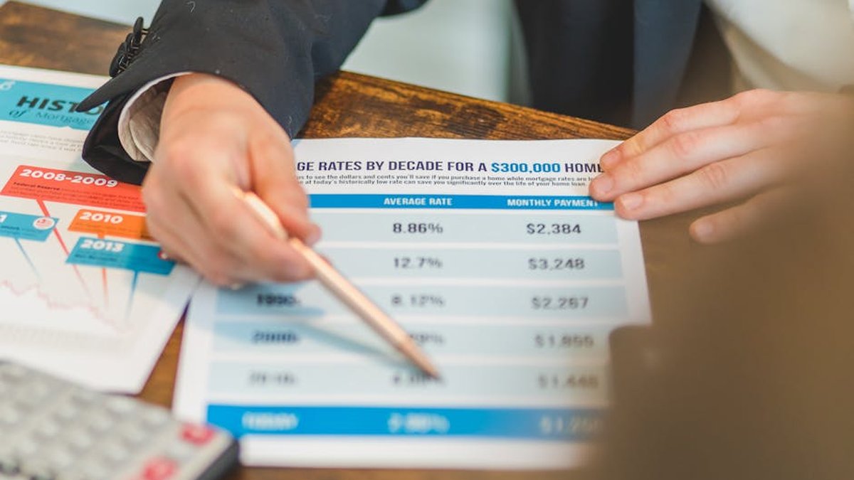 A close-up of hands analyzing mortgage rate documents with a pen and calculator in a business setting.