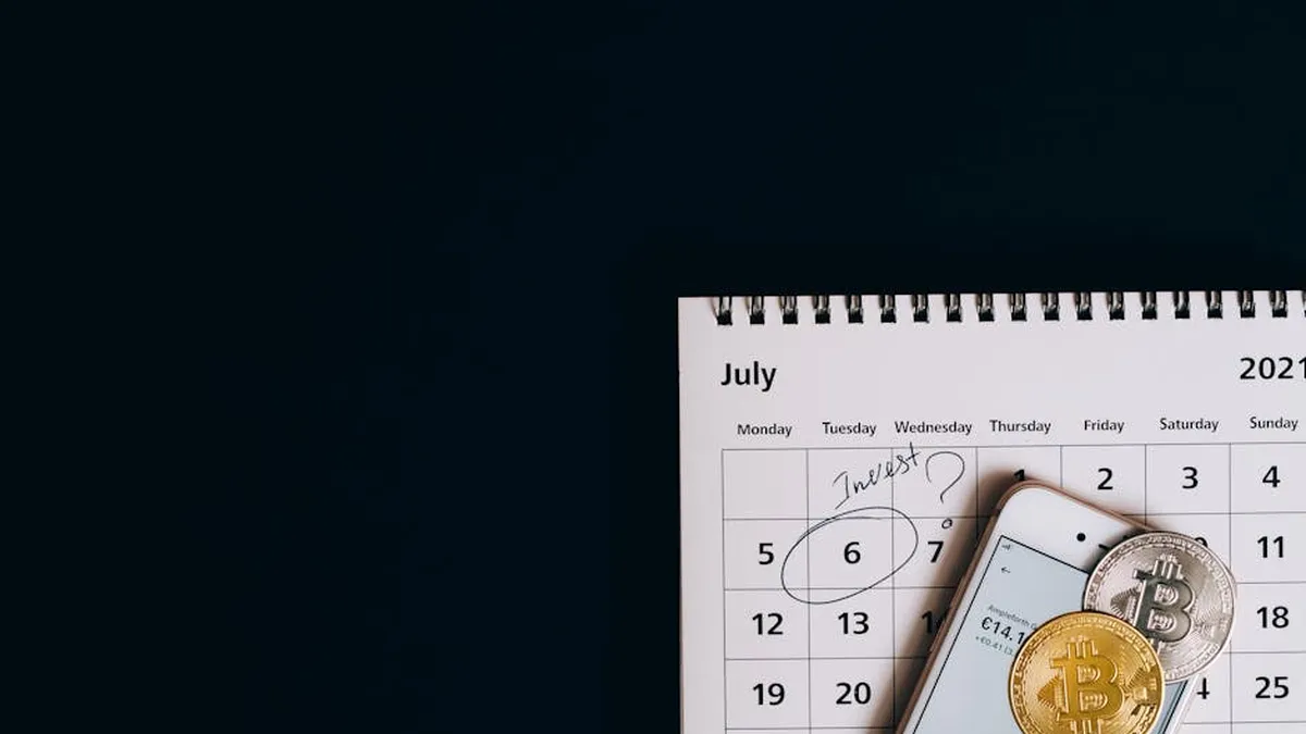 Top view of bitcoins and smartphone on July 2021 calendar, suggesting investment planning.