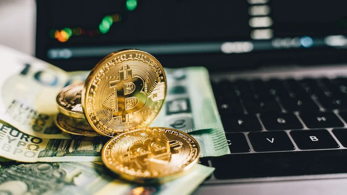 Bitcoin coins and Euro banknotes on a laptop with stock graph in background.