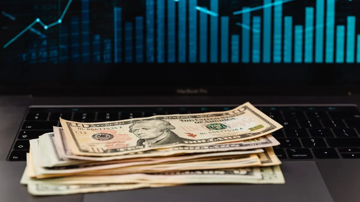 US dollar bills on laptop with financial graph in background, symbolizing wealth and technology.
