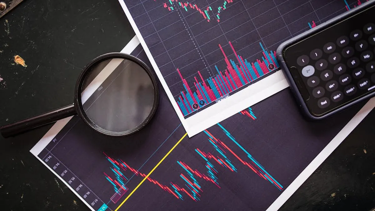 Stock market charts analyzed with a magnifying glass and calculator for financial research.
