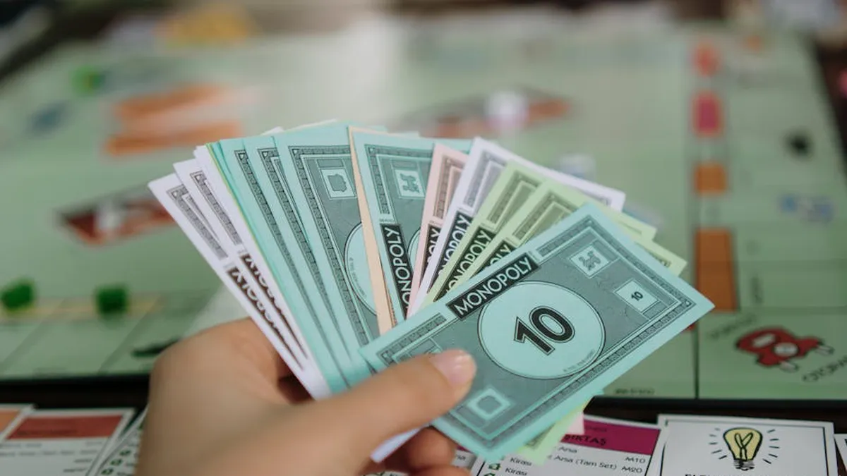 Close-up of a hand holding Monopoly money with board game in the background.