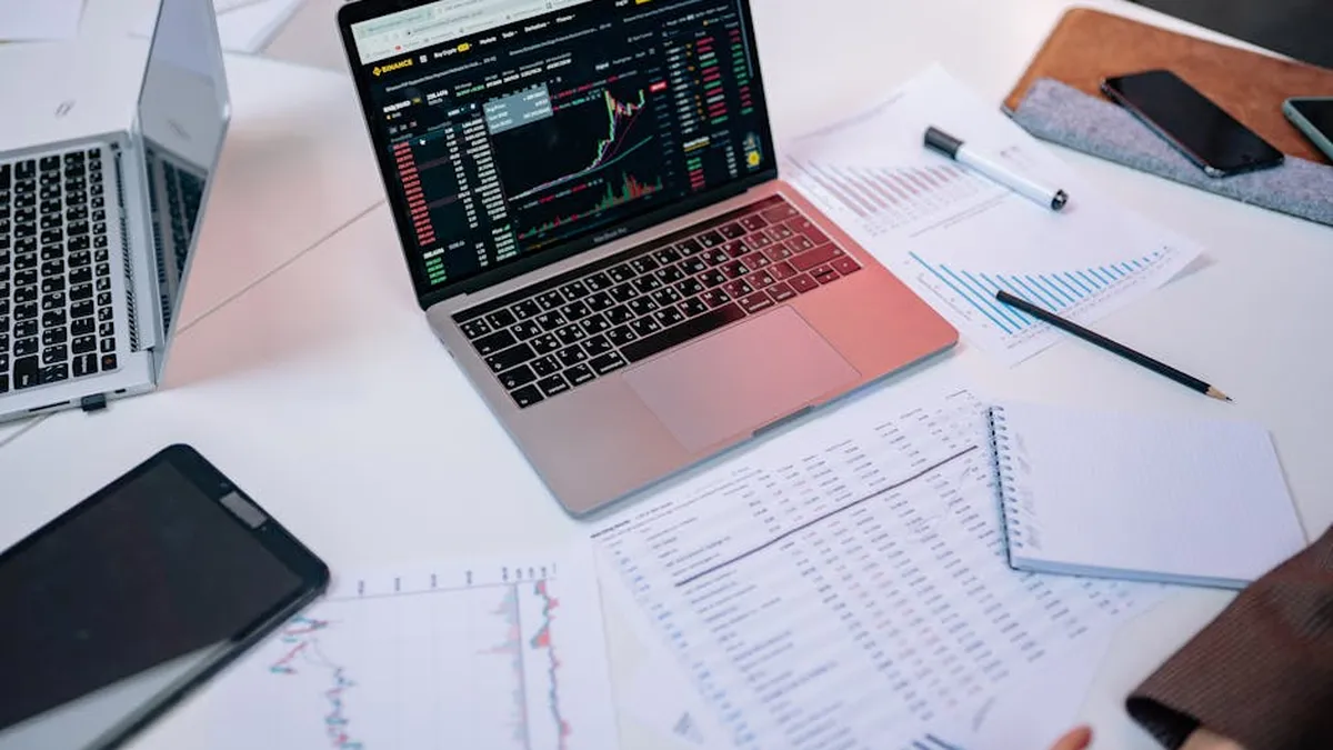 Laptops on a desk displaying stock market charts and financial documents.