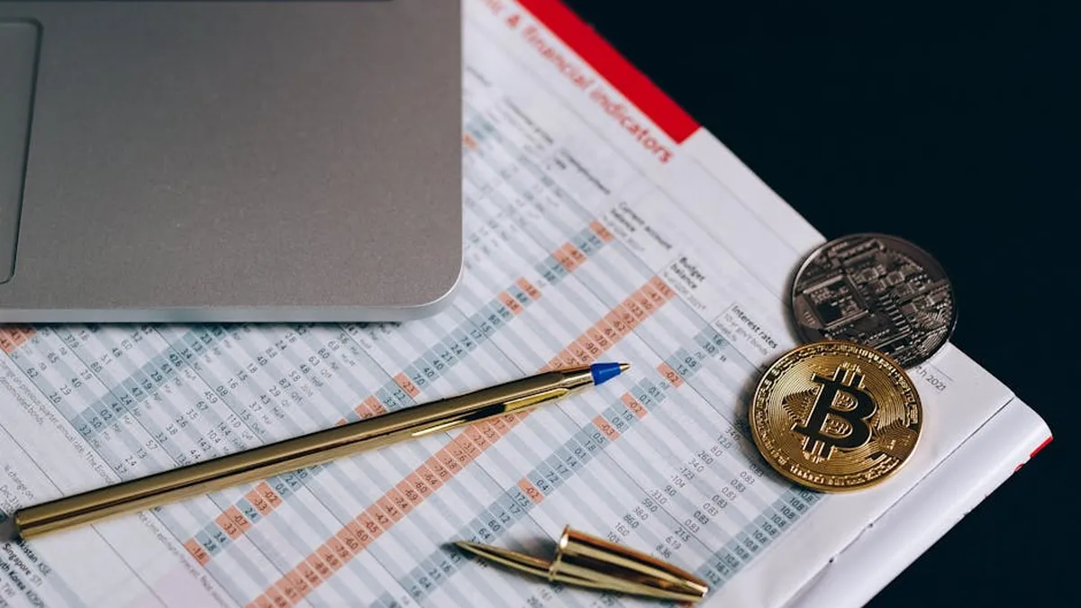 Flat lay of Bitcoin coins on a financial report with a laptop and pen.