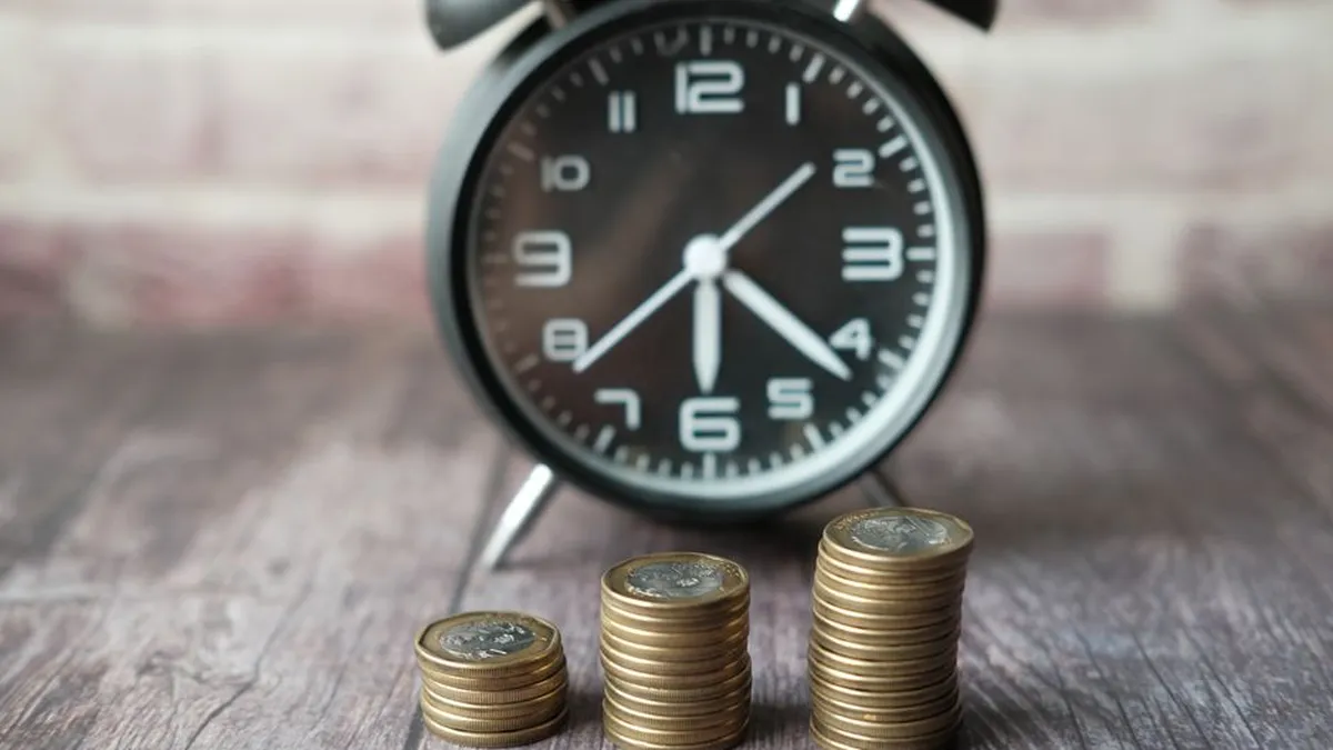 Stacked coins and a classic alarm clock symbolize the value of time and money.