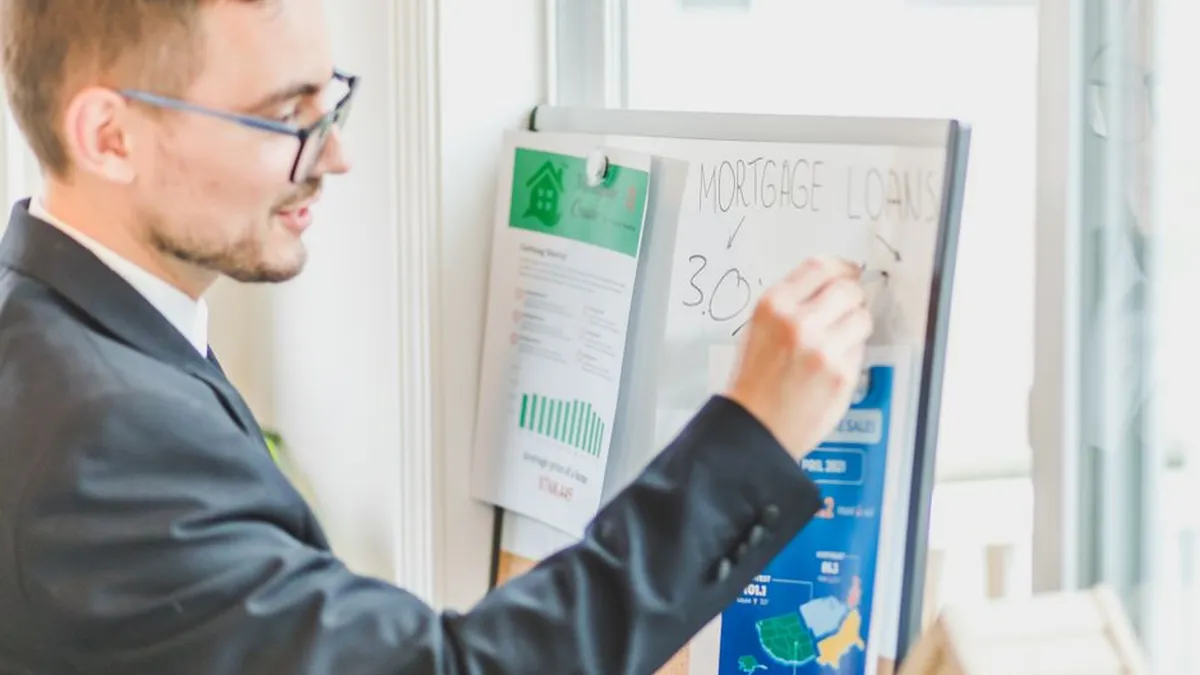 Businessman in suit writes on whiteboard displaying mortgage loan rates during a real estate meeting.
