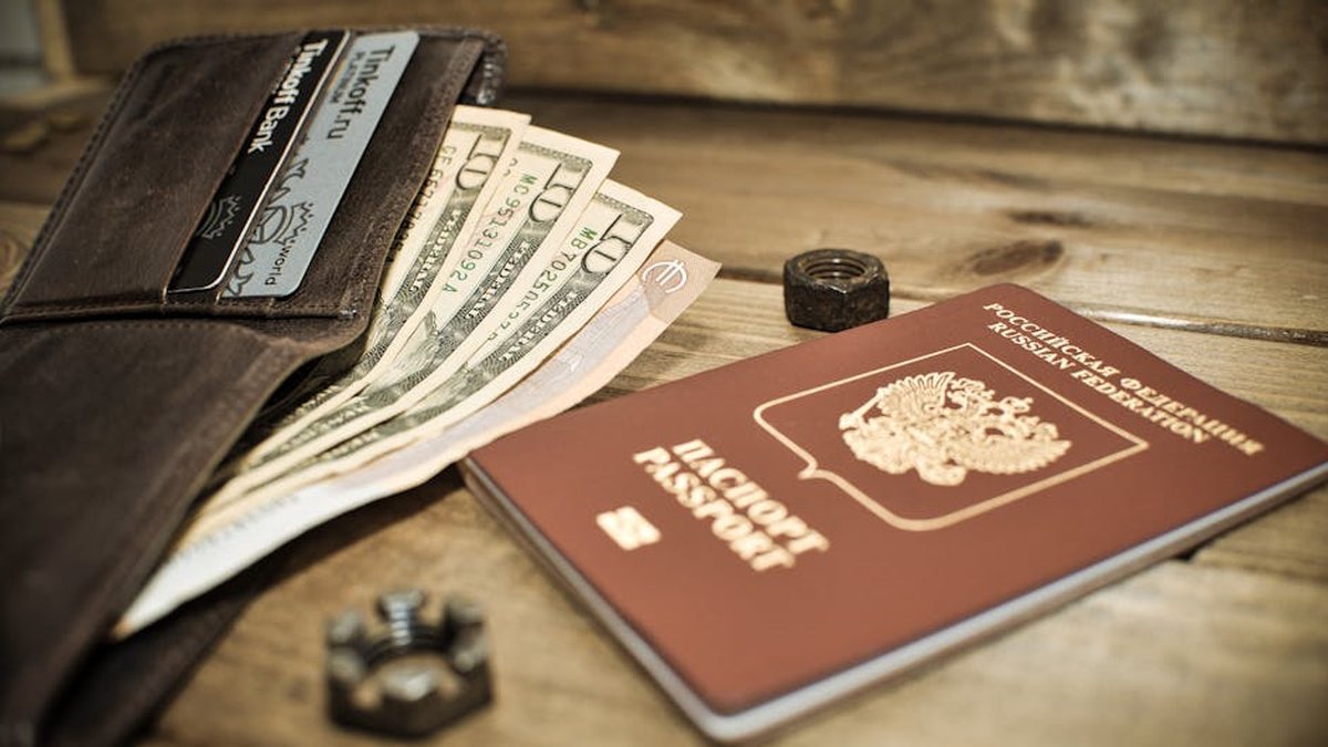 A wallet with cash, credit cards, and a Russian passport on a wooden table.