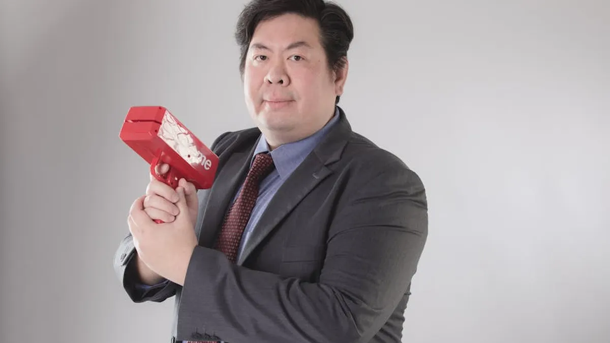 Confident businessman posing with a red money gun in a studio setting, wearing a formal suit.