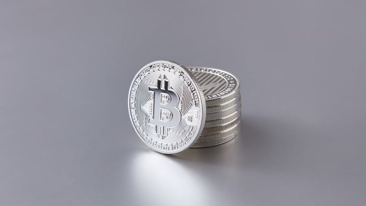Stack of silver Bitcoin coins on a smooth gray surface, representing digital currency.