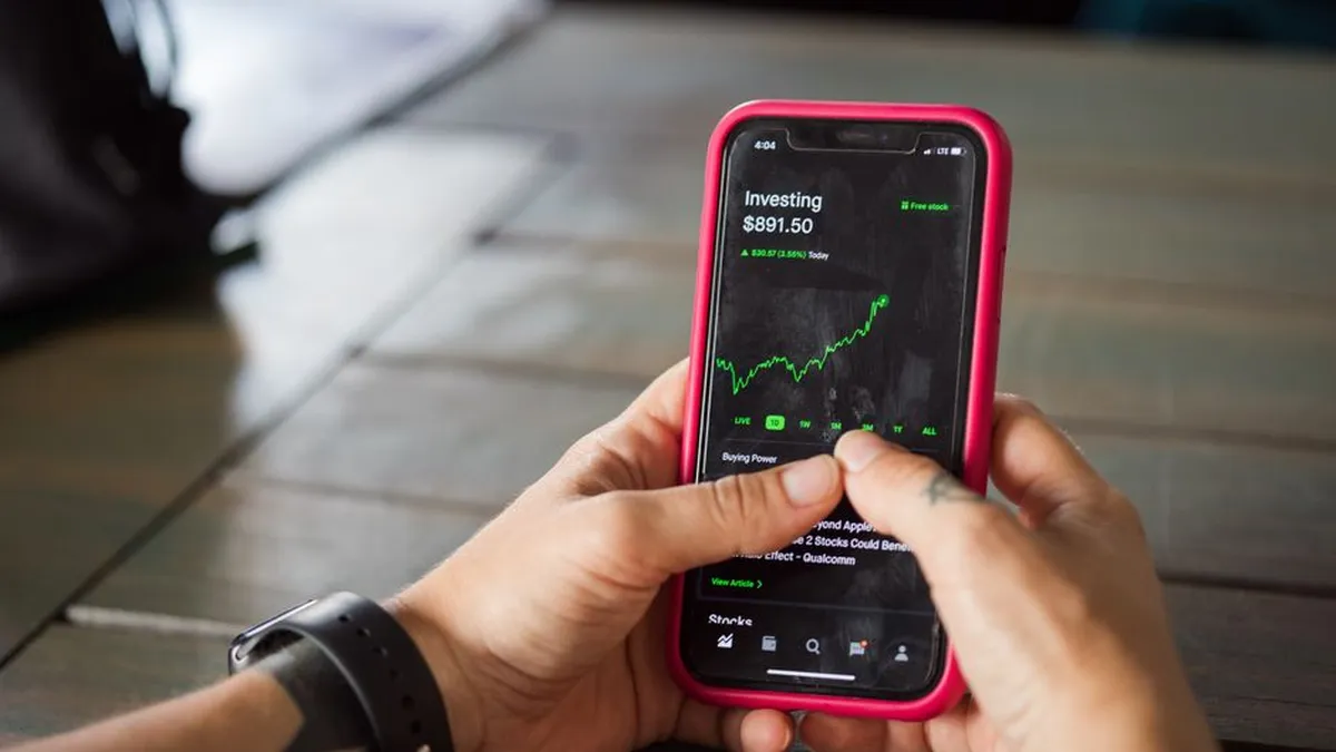 A person holding a smartphone with a stock market app displaying analytics and stock prices.