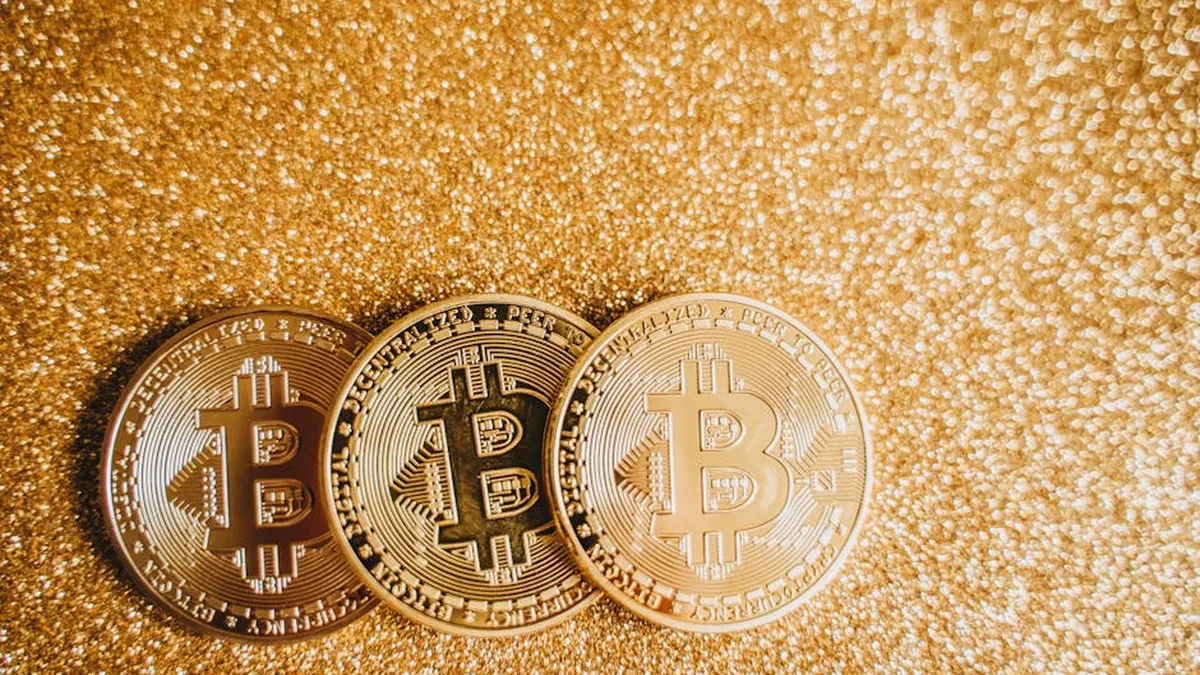 Close-up of three shiny Bitcoin coins on a sparkling gold glitter background, symbolizing cryptocurrency wealth.