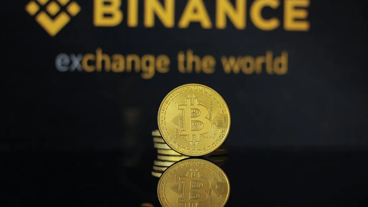 Close-up of a Bitcoin coin with Binance logo and text reflecting in dark surface.