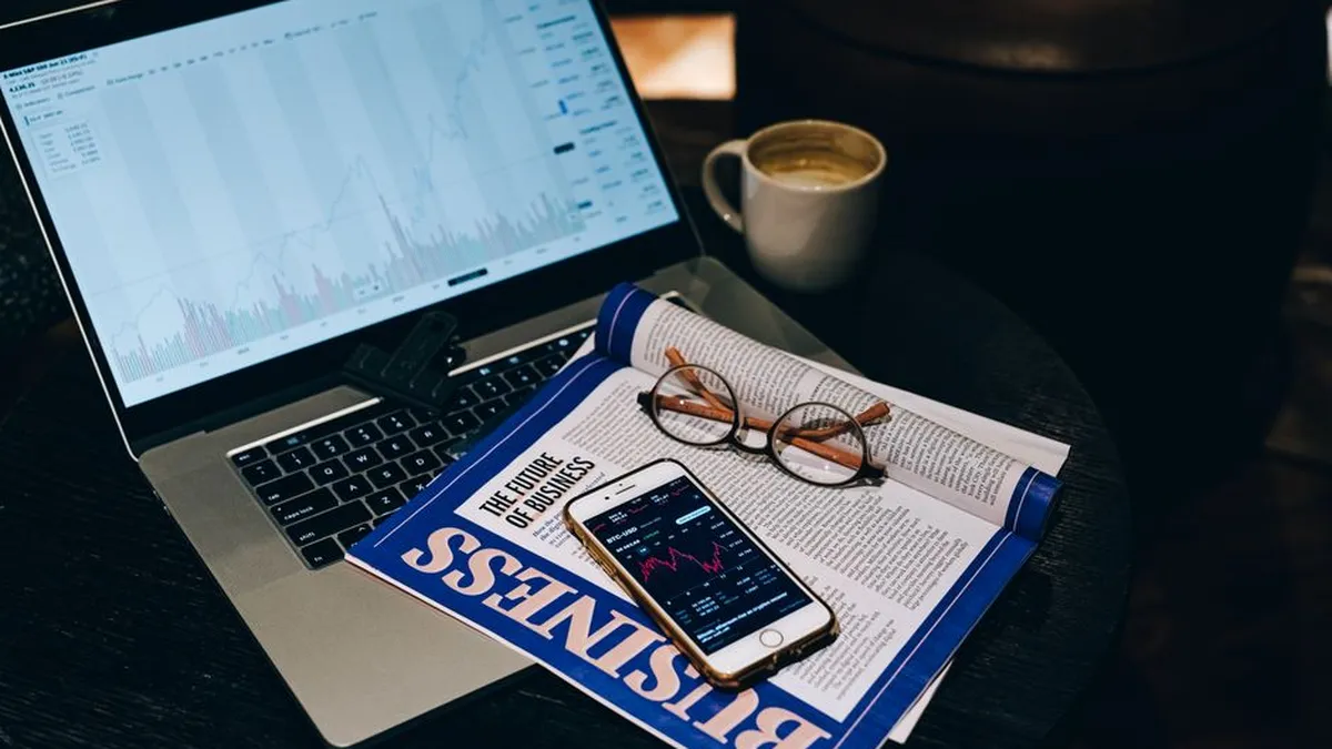 A professional workspace featuring a laptop, smartphone, coffee cup, and business magazine on a table.