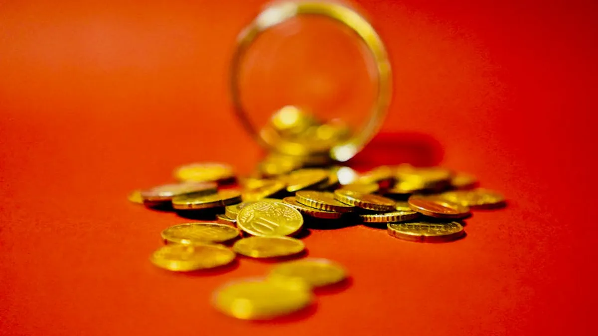 A collection of golden coins spilling from a glass jar on a vibrant red background symbolizes wealth.