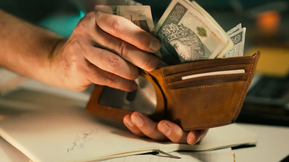 A close-up of hands holding a wallet filled with Polish banknotes on a desk.