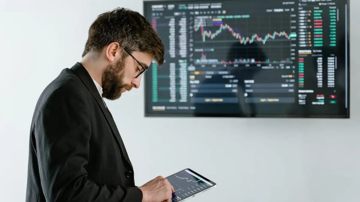 Professional man using tablet in front of cryptocurrency trading screen indoors.