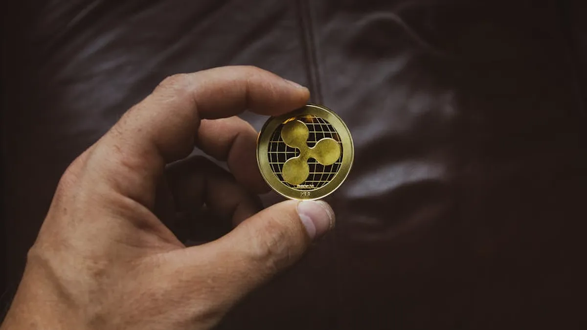 A close-up of a hand holding a gold Ripple cryptocurrency coin, symbolizing digital currency concept.
